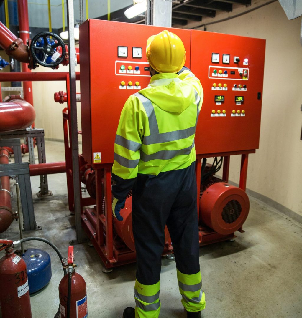 Worker in safety gear operates electrical control panel in industrial setting.