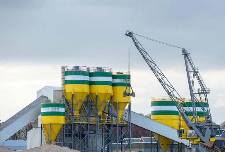 A large industrial crane working with silos at a modern cement plant under cloudy skies.